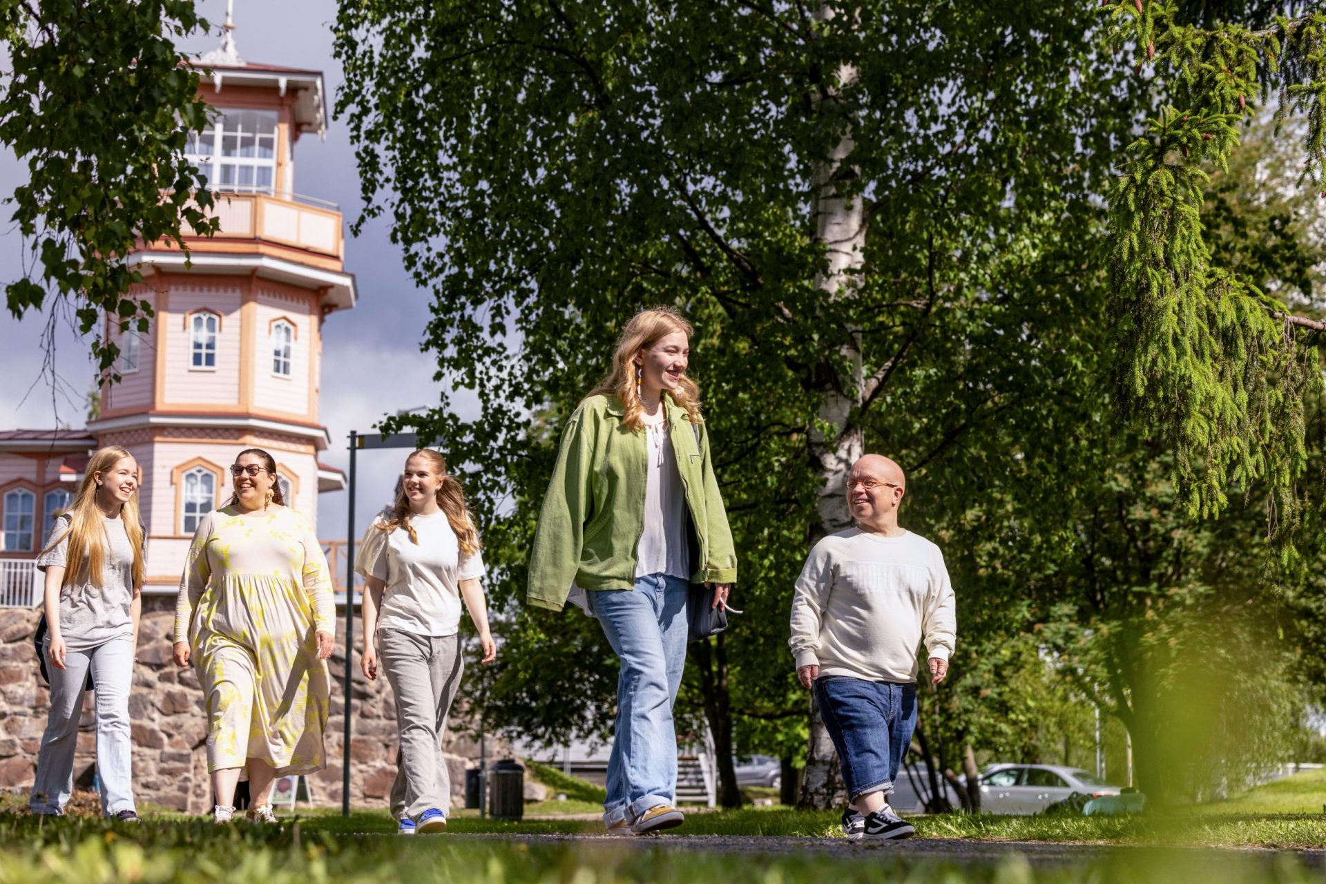 People walking in summer. In the background, there is pink wooden castle and green trees.